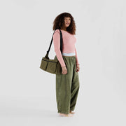 A person holding a Baggu Large Cargo Crossbody bag in Seaweed over their shoulder