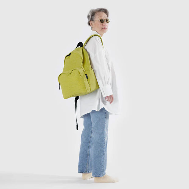 A person wearing a large recycled nylon backpack from BAGGU in Lemongrass over their shoulder
