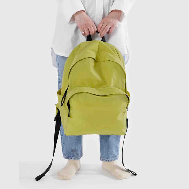 A person holding A large recycled nylon backpack from BAGGU in Lemongrass by its strap