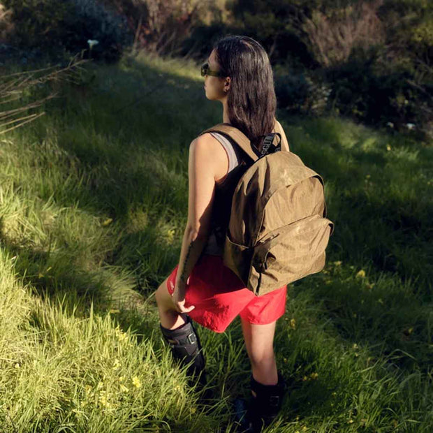 Person walking through a grassed area wearing A large recycled nylon backpack from BAGGU in the Seaweed colour way on their back