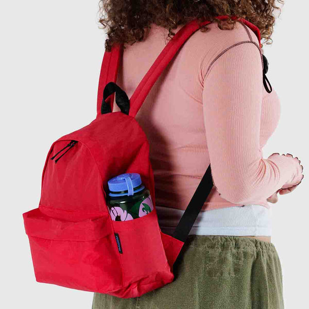 A person wearing a medium recycled nylon backpack from BAGGU in Candy Apple on their back