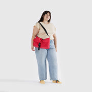 A person wearing a Baggu Recycled Nylon Messenger Bag in Candy Apple over their shoulder