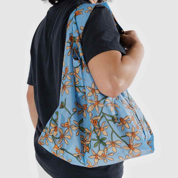 A Standard Baggu reusable bag in the Orchid design worn over a person's shoulder