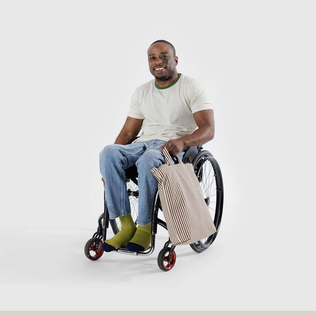 a person in a wheelchair holding a A Baggu Zip Duck Bag in Brown Stripe design