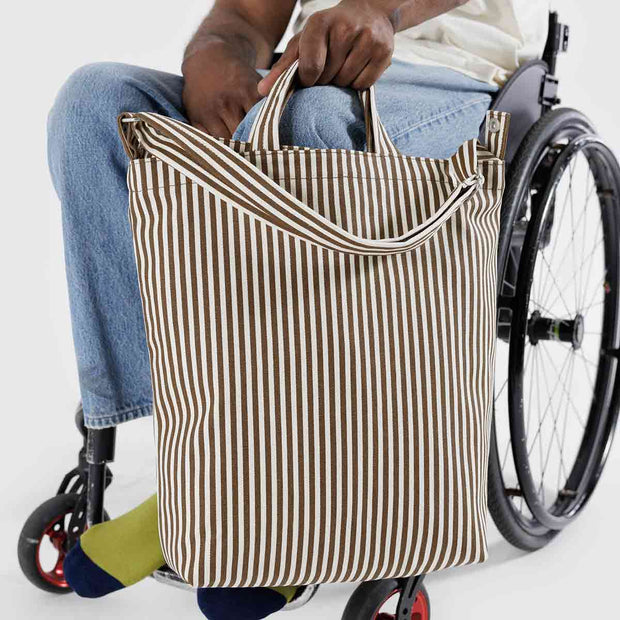Close up of a person in a wheelchair holding a A Baggu Zip Duck Bag in Brown Stripe design