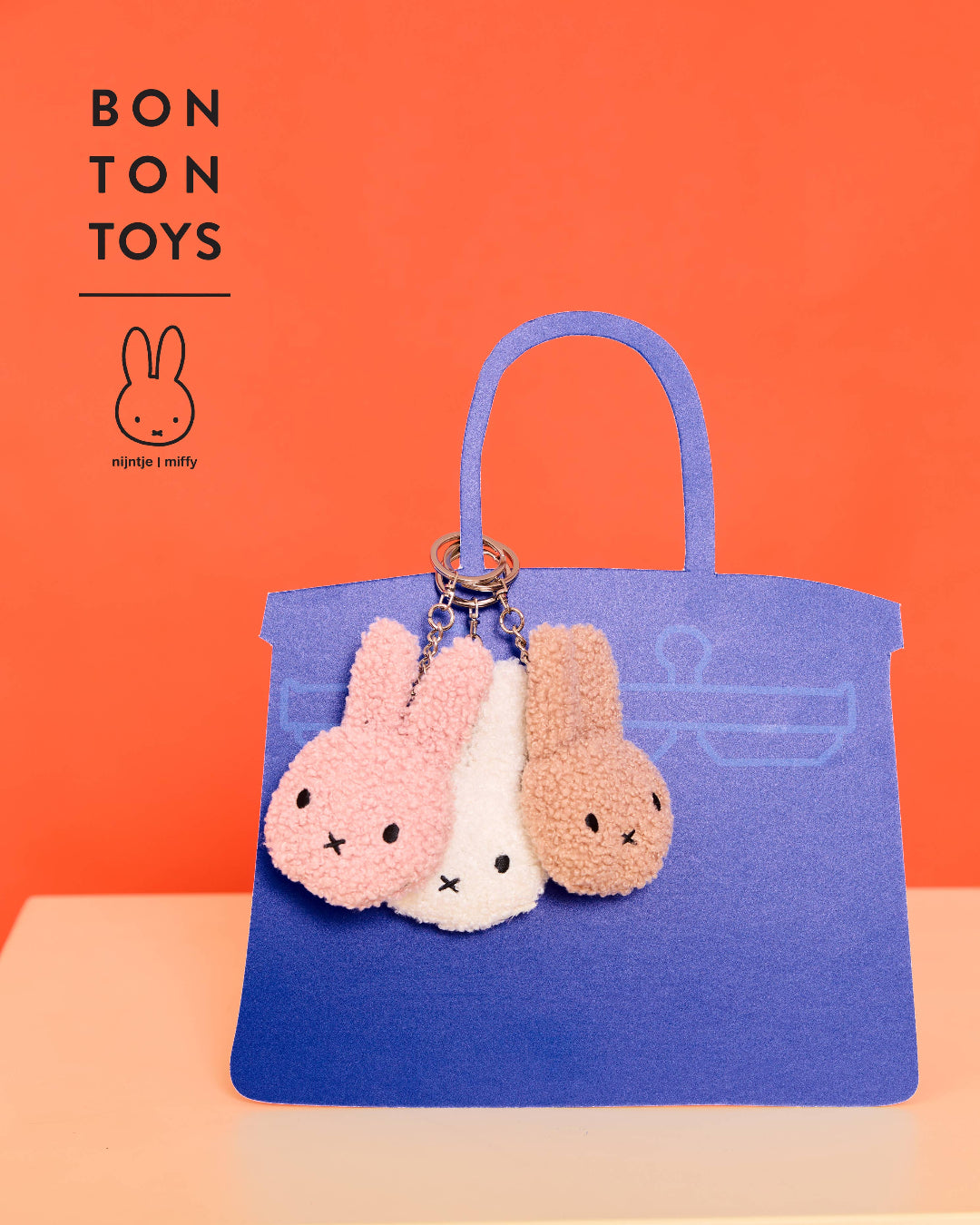 Blue handbag with three fluffy Miffy keychains on an orange background, featuring the Bon Ton Toys brand.