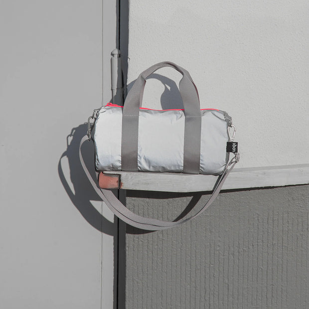 A lifestyle image of a  a reflective Neon Dark Orange Mini Weekender from LOQI sat on a shelf