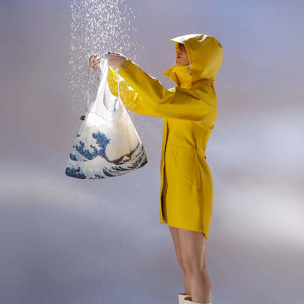 A person in a yellow macintosh holding a LOQI x Katsushika Hokusai recycled shopping bag featuring The Great Wave