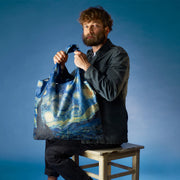 A man sat holding a A Vincent Van Gogh recycled shopping bag featuring The Starry Night