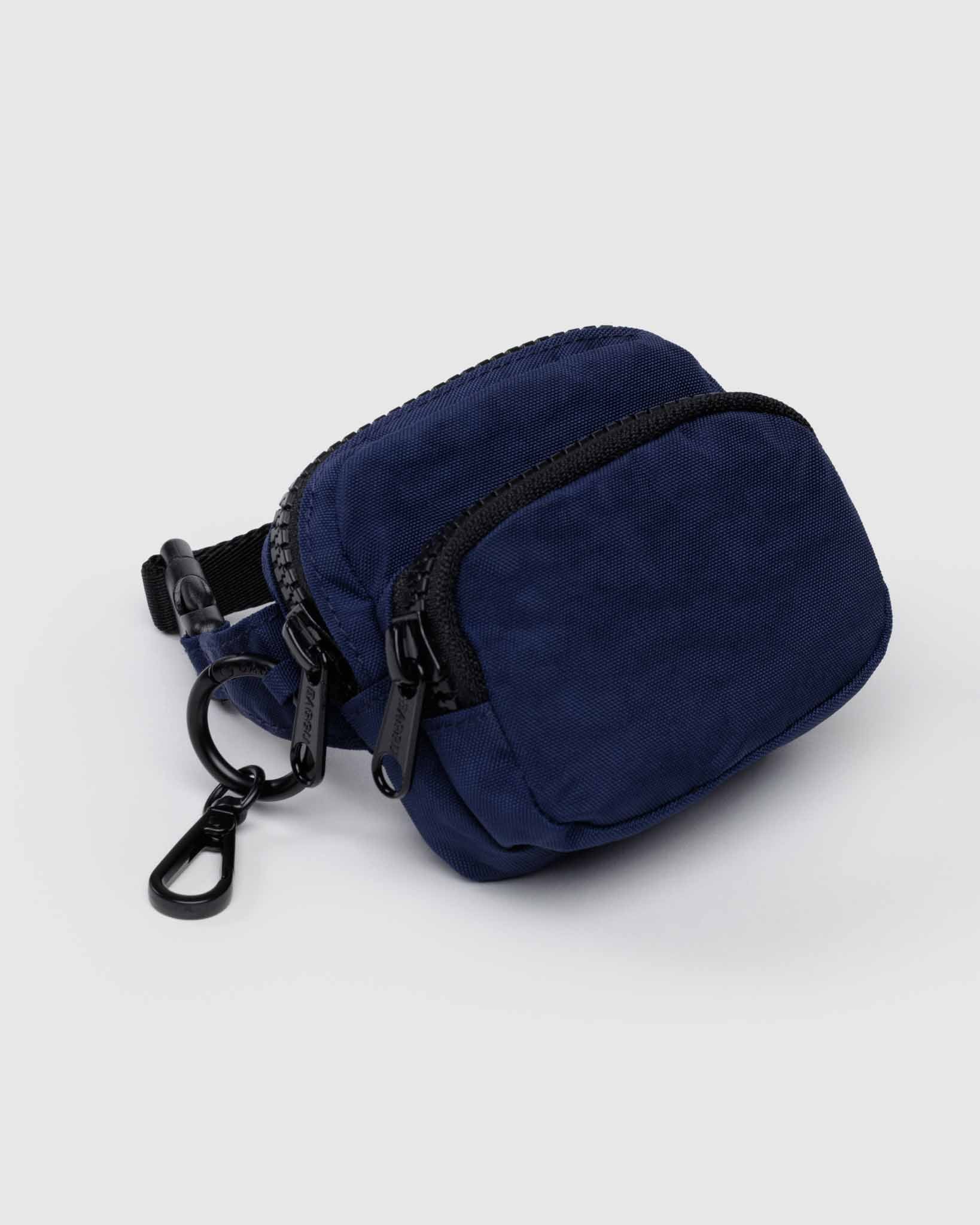 Navy blue BAGGU fanny pack charm pouch with black zipper and clasp on a light gray background