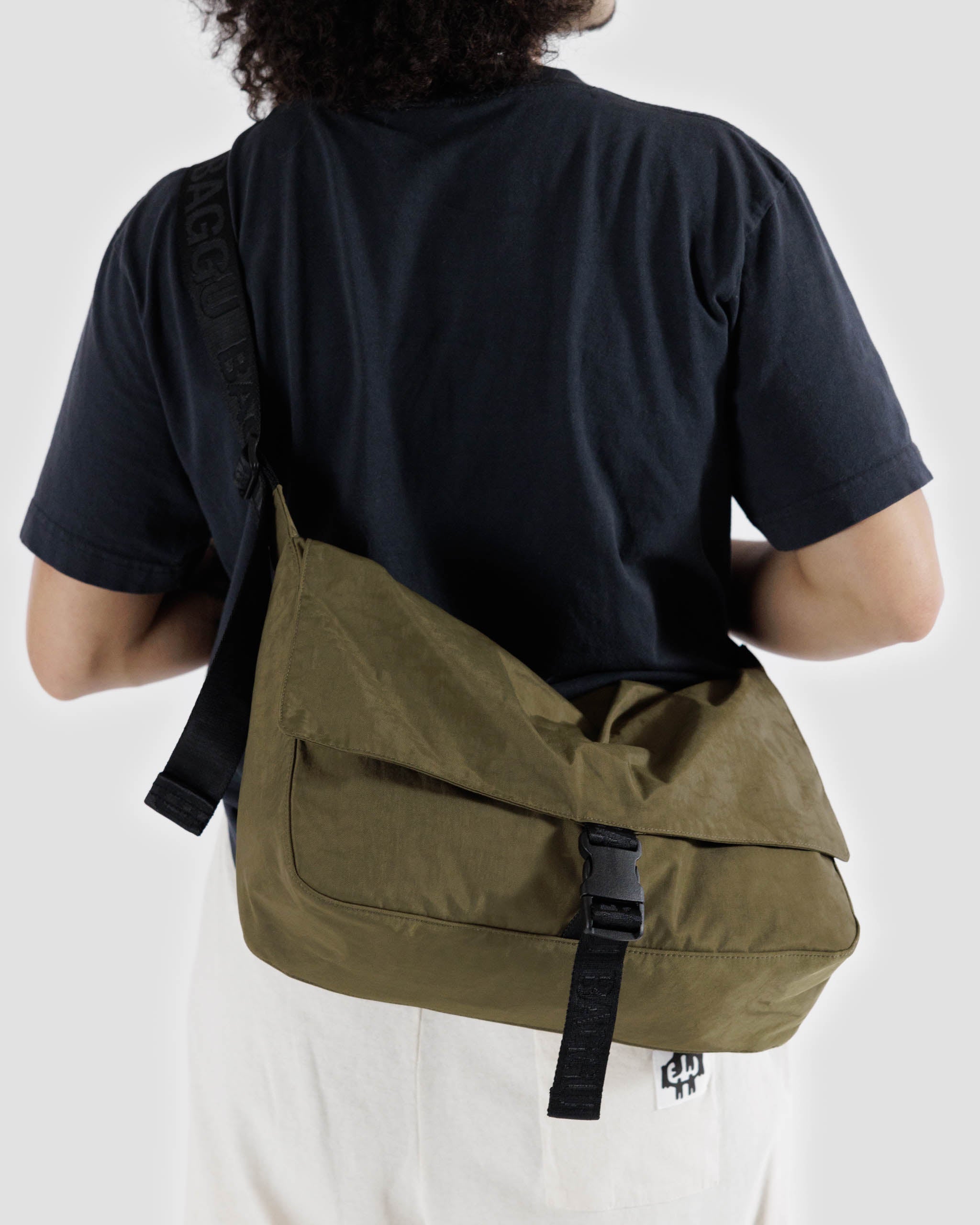A close up of a person holding a BAGGU nylon messenger bag in Seaweed