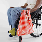 A person in a wheelchair holding a Baby Baggu featuring the Red Gingham design