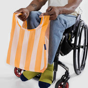 A person sat in a wheelchair holding A Baby Baggu featuring the Tangerine Wide Stripe design