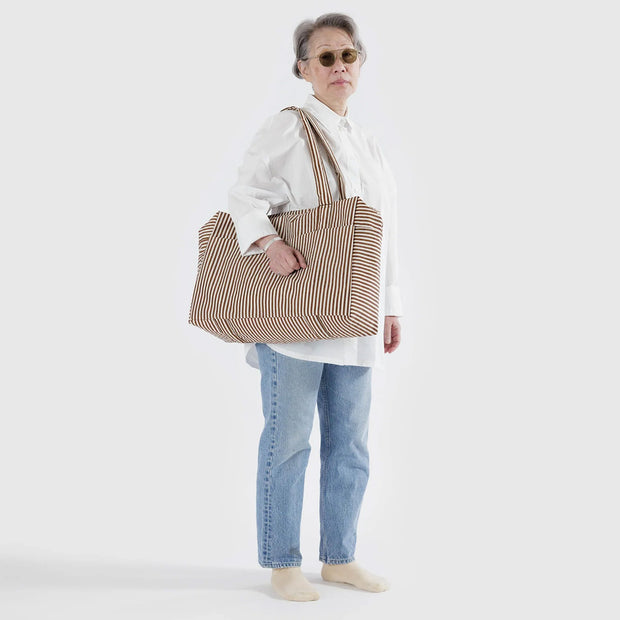 A person holding a Baggu Cloud Carry-On in Brown Stripe