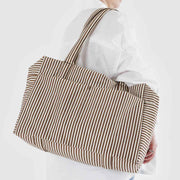 A person holding a Baggu Brown Stripe Cloud Carry-on bag