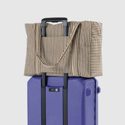 A Baggu Cloud Carry-On in Brown Stripe hooked over a suitcase