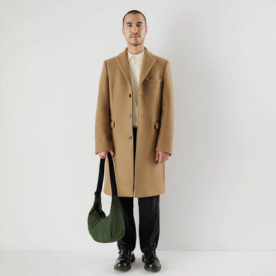 Man in camel coat holding a medium Bay Laurel Baggu crescent bag