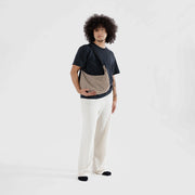 A person holding a Baggu medium Crescent Bag in Brown Stripe