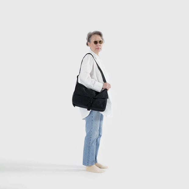 A person holding a Baggu Recycled Nylon Messenger Bag in Black over their shoulder