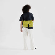 A person shown from the back with a Baggu Recycled Nylon Messenger Bag in Lemongrass worn crossbody
