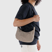 A close up of someone wearing a small Crescent Bag from Baggu in Brown Stripe over their shoulder