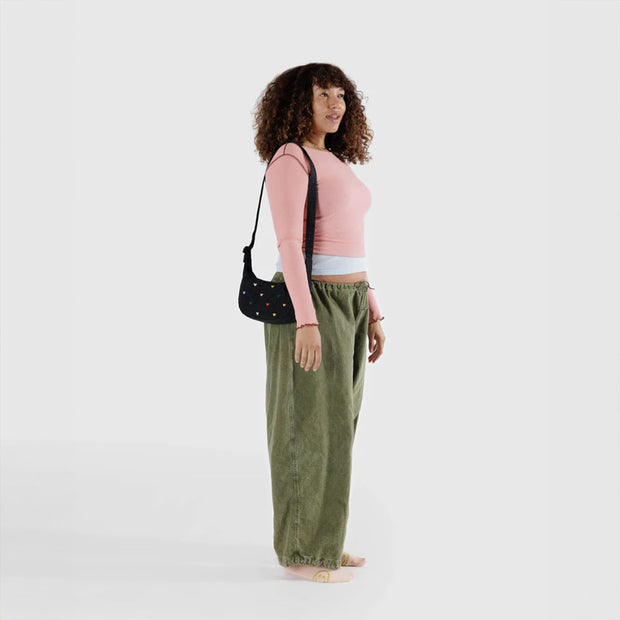 A person wearing One small Crescent Bag from Baggu in Embroidered Hearts over their shoulder