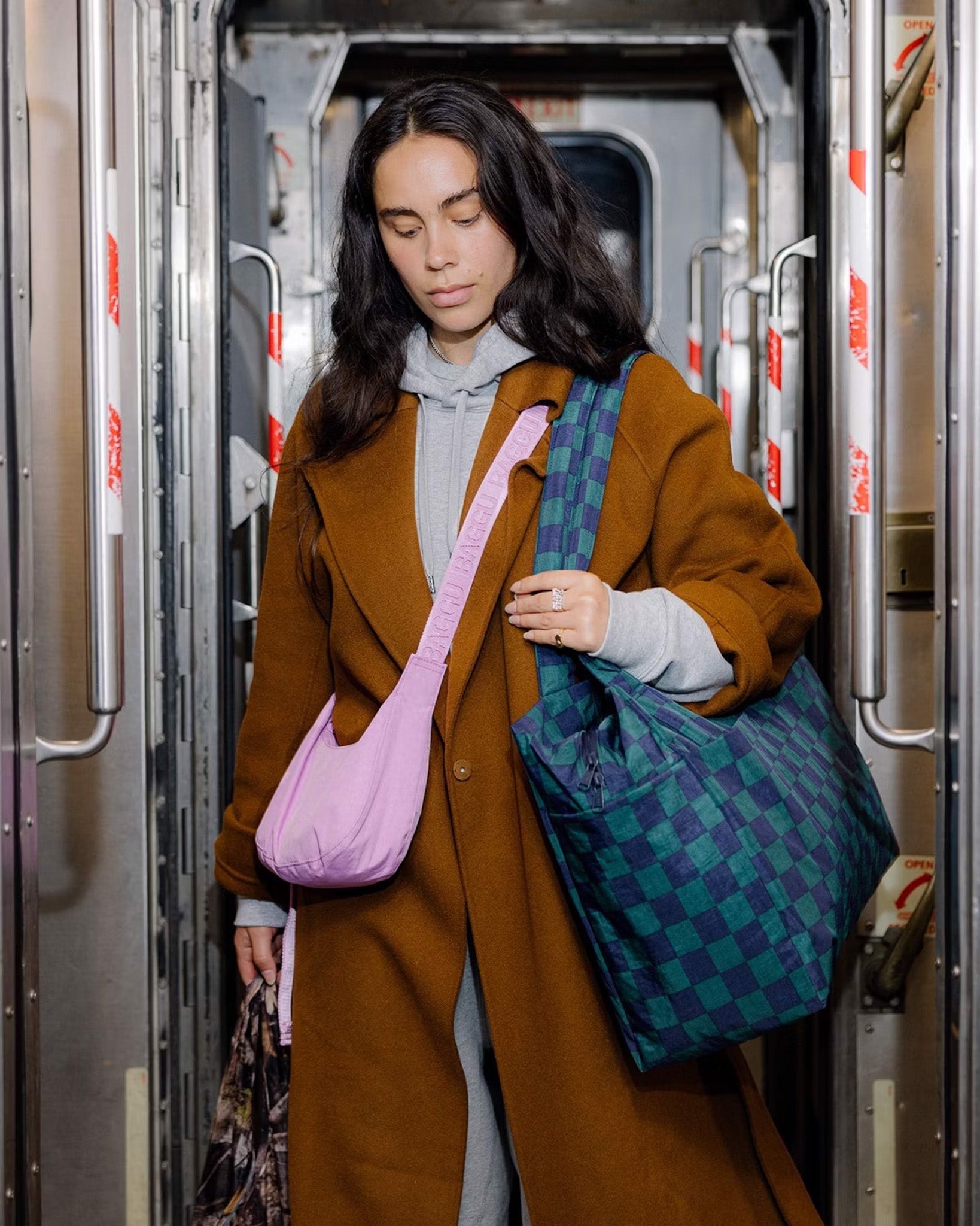 A person wearing a BAGGU small crescent bag in Peony navy and green check cloud carry-on