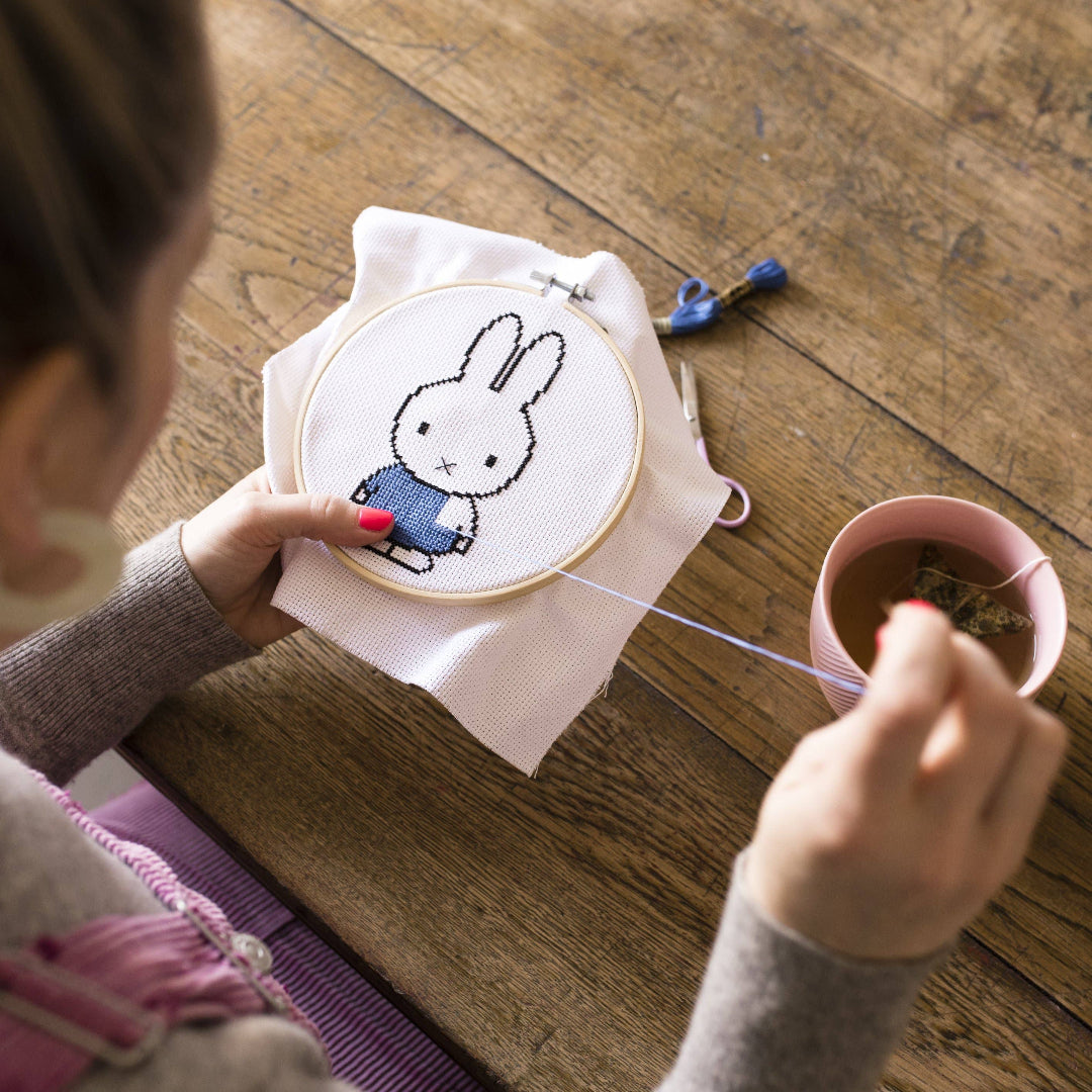 Person holding a cross-stitched Miffy bunny in an embroidery hoop.