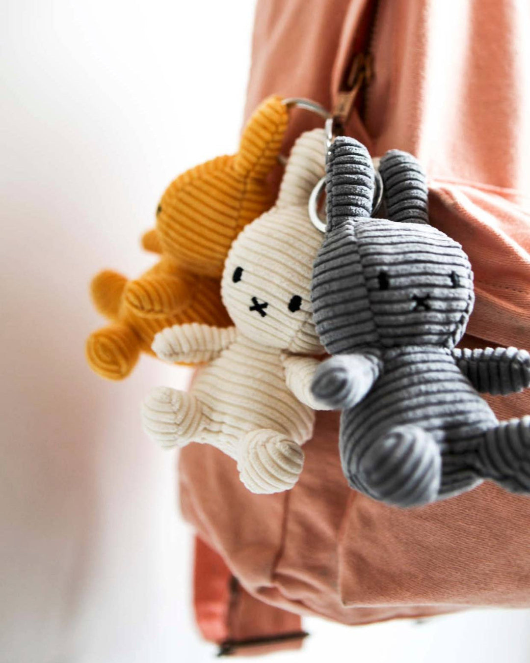 Three plush miffy keychains, one grey and one white, hanging from a pink bag.