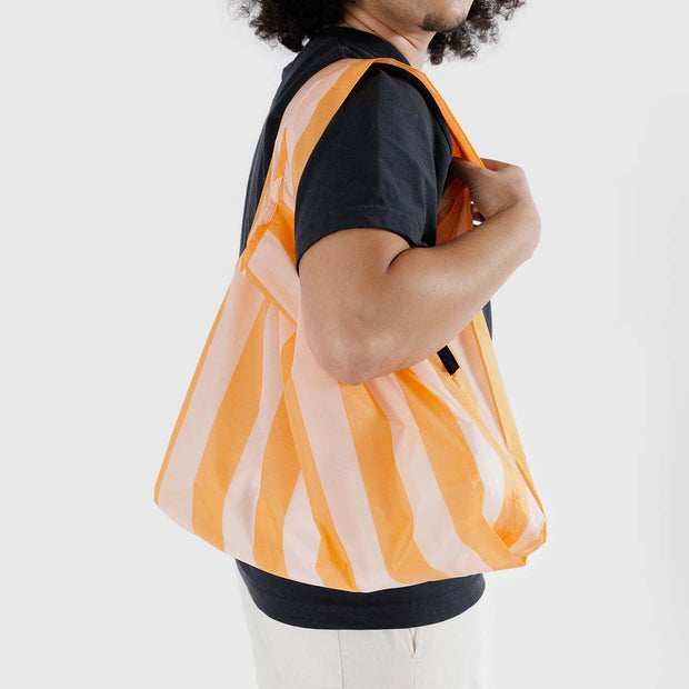 A person wearing a Baggu Tangerine Wide Stripe standard reusable bag over their shoulder