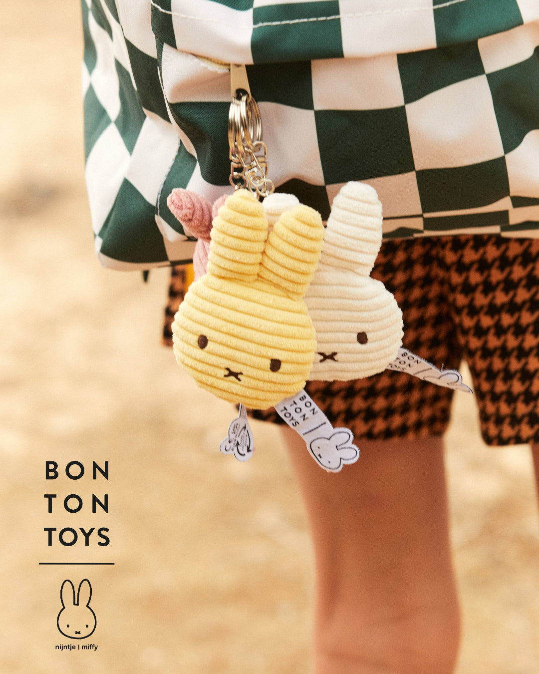 Two plush Miffy keychains, with a person wearing checkered pants in the background.